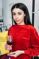 beautifiul african american girl holding glass of wine and looking at camera