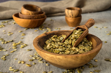 Pumpkin seeds with a bowl and scoop on a wooden background.
