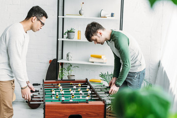 multicultural friends playing table football in spacious living room