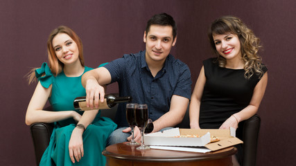 One man in the company of two women party, alcohol. Girls seduce a man having fun and drinking wine, eating pizza.