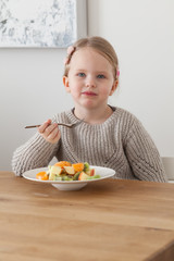 Cute little girl eating a fruit salad in design dining room. Child having a dinner at home. Healthy nutrition for small kids.