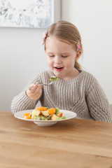 Cute little girl eating a fruit salad in design dining room. Child having a dinner at home. Healthy nutrition for small kids.