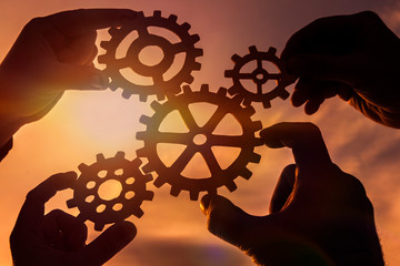 gears in the hands of a group of people at sunset. mechanism, the concept of teamwork.