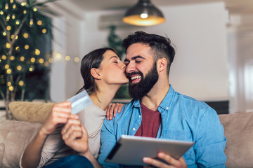 Smiling couple using digital tablet and credit card at home