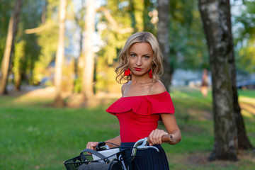 Fototapeta na wymiar A young blonde woman with a bike in the park - image
