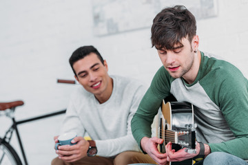 handsome young man playing guitar to mixed race friend