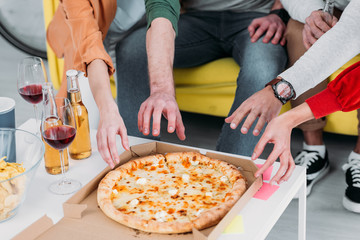 cropped view of men and women stretching hands to pizza