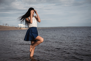 Brunette girl in a skirt standing in the water with her hair down. against the background of concrete and hydroelectric power. dramatic light.