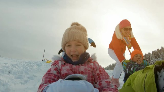 Parents pushing their children on sleds down a snowy hill in slow motion
