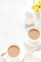 Breakfast on white background. Morning coffee with cream, pie and yellow flowers. Top view, copy space