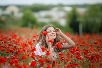 Beautiful happy smiling teen girl portrait with red flowers on head enjoying in poppies field nature background. Makeup and curly hair style. Lifestyle.