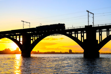 Fototapeta na wymiar Silhouette of arched railway bridge and a train on the Dnieper river at beautiful sunset. Dnipo city, Dnepropetrovsk, Ukraine.