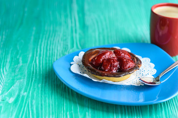 A cupcake with a strawberry, next to coffee in a red cup, photographed on a wooden background.