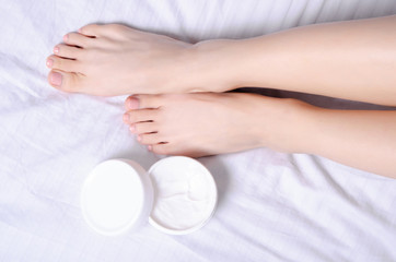 Fototapeta na wymiar Female legs feet heel foot white jar cream in white bed, top view