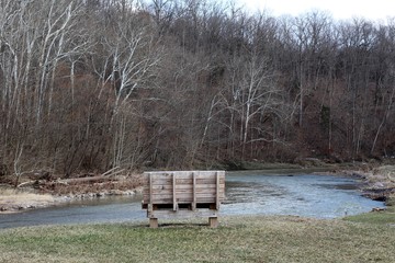 A empty wood park bench with a view of the creek.
