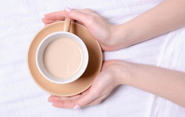 Woman holding cup of coffee in the white linens bed, top view