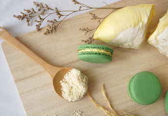 Durian macarons in green and yellow colors with dry flowers and almond powder on wooden breadboard