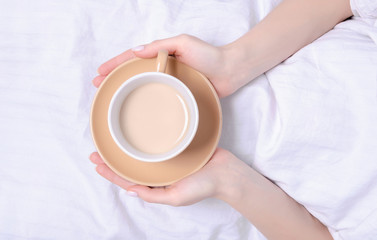 Woman holding cup of coffee in the white linens bed, top view