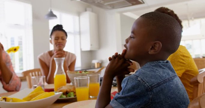 Black family praying together before meal on dining table 4k