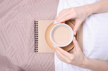 Woman in the white bed cup of coffee in hand notebook brown blanket, top view