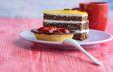 A cupcake with strawberries and a puffy biscuit cake on a plate, next to coffee in a cup, photographed on a wooden background.