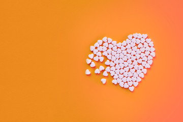 White heart shaped candies on an orange paper background. Broken heart or pearts gethering love concept. Copy space included.