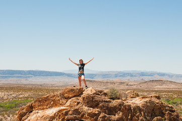 A woman standing on a rock with lifted hands up over the mountains of a Texas desert