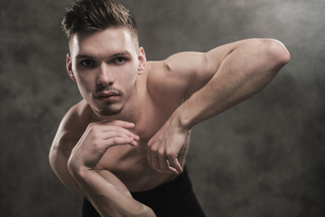 A young male ballet dancer with black leggings and a naked torso performs dance moves against a...