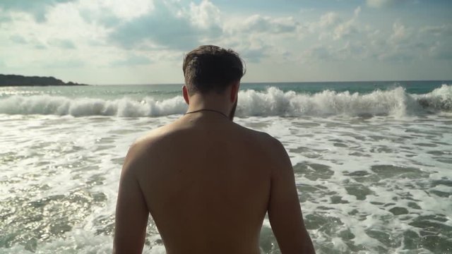Mans shirtless back near amazing blue sea, vawes splashes