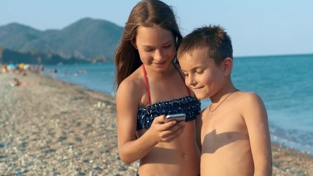 Children looking photo on smartphone at sea beach. Boy with girl reviewing photo