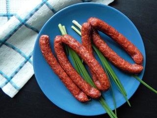 Smoked sausages with  green onions and half of red onion on blue plate