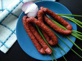 Smoked sausages with  green onions and half of red onion on blue plate