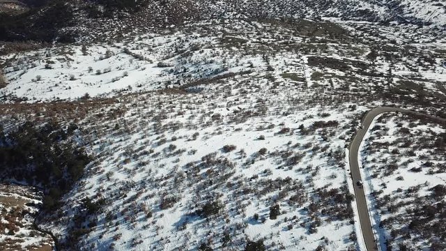 top view aerial drone flying above curvy road wind mountains and forest covered with snow on bad weather.