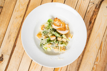Fresh caesar salad in white plate, wooden background