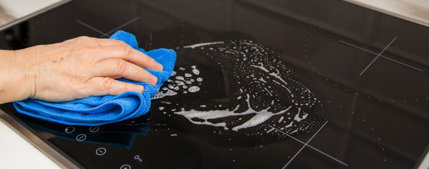 A woman's hand with a blue microfiber cloth rubs a glass ceramic stove in the kitchen.