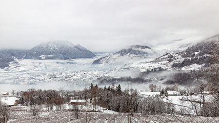 Fototapeta na wymiar Cold foggy winter day in Valsugana, Sugana Valley, seen from Strigno, located at the Alps’ foothills in Trentino, Italy. Mystic landscape of the Dolomite mountains.