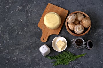 Ingredients for cooking baked champignons with suluguni on a dark gray background: raw champignon mushrooms, suluguni cheese, dill, butter, salt, pepper. Georgian cuisine. Top view.