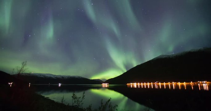northern lights time lapse reflecting in the water of a Fjord in Norway in green blue and violette colours 