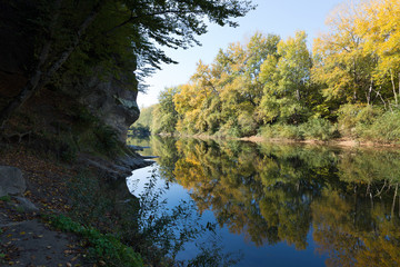 Bright yellow-green trees with reflection on the smooth surface of a mountain river. Beautiful landscape.
