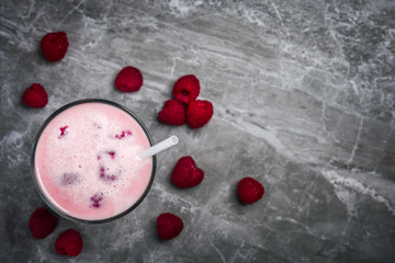 A glass of dairy free milkshake with fresh organic raspberries on a marble stone background with copy space