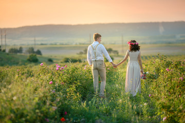 The girl in the hands holding a gift, a bouquet of flowers, from roses.  Against a beautiful landscape. Happy young couple newlyweds, romantic family. walking at sunset in a wheat field.