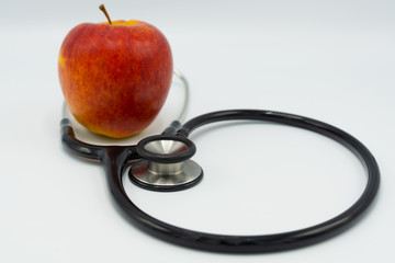 Black stethoscope and red apple on white background