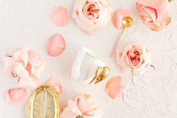 Stylish coffee or tea set on pastel background with pink flowers, leaf golden plate and spoon with roses and petals. Flatlay, top view on pastel concrete background