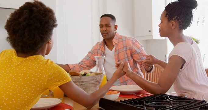 Black family praying together before meal on dining table 4k