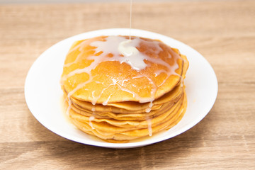 Pancakes with condensed milk on a white light background. A stack of pancakes with sweet sauce. Close up view.