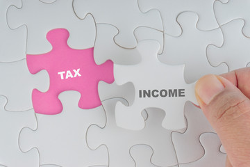Fototapeta premium Hand holding piece of jigsaw puzzle with word INCOME TAX. Selective focus