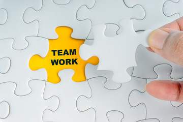 Fototapeta premium Hand holding piece of jigsaw puzzle with word TEAMWORK. Selective focus