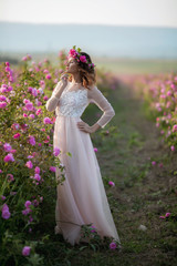 Fototapeta na wymiar Young beautiful girl in a long dress and a wreath of flowers in the garden of lilac bush