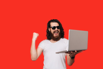 Young bearded mna using computer laptop very happy and excited, winner expression celebrating victory screaming with big smile and raised hands