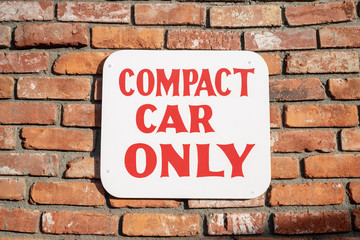 COMPACT CAR ONLY sign red lettering on white mounted to red brick wall